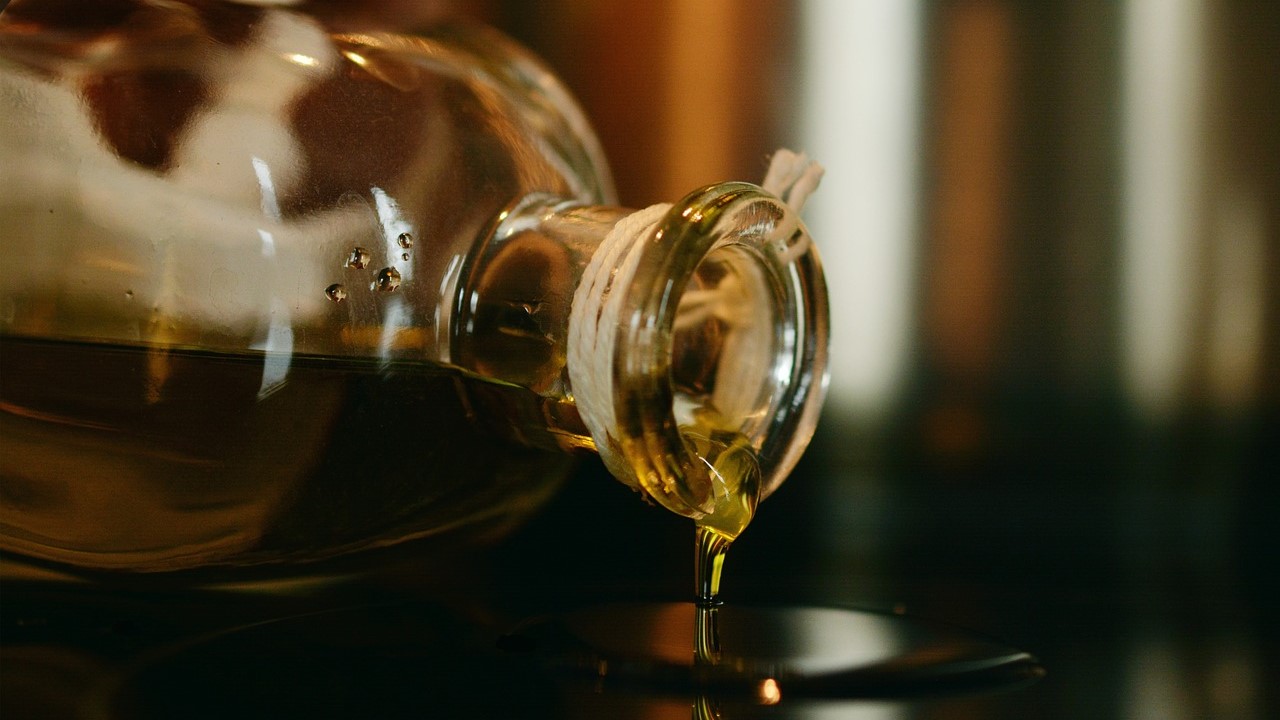 oil is being poured out of a glass jar